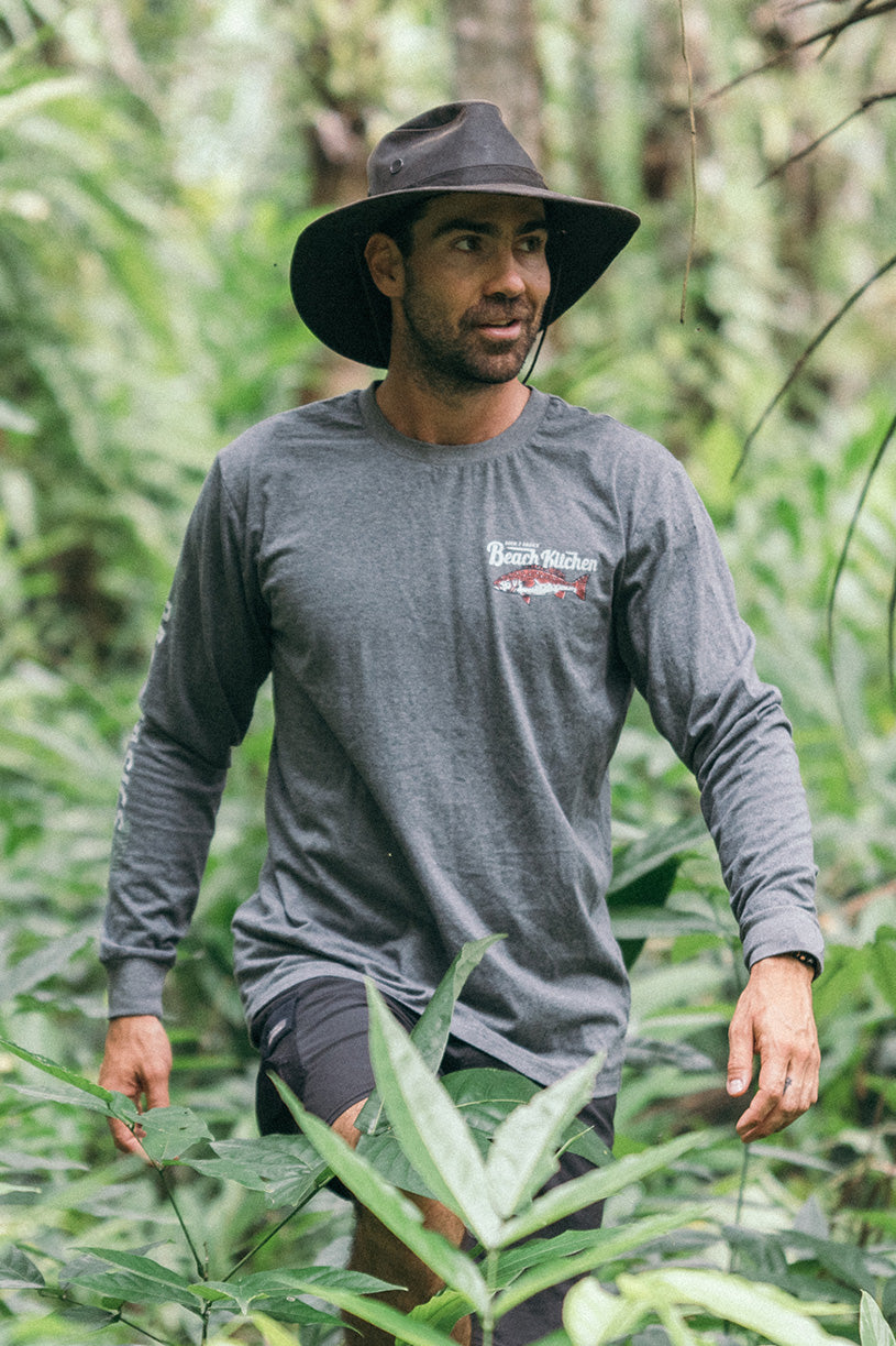 az walking in the forest wearing a long sleeve grey marle tee shirt with a picture of a fish being cooked on a beach bbq by back 2 basics adventures