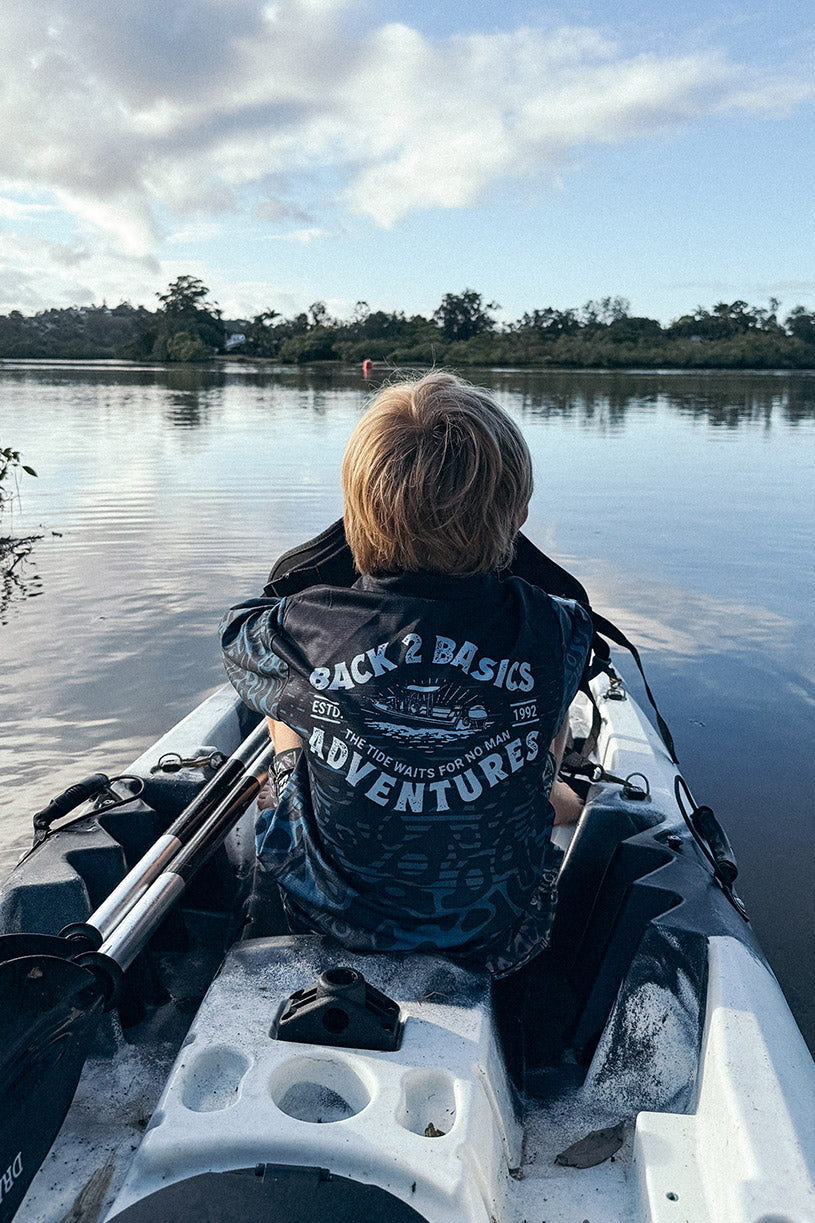 Kid wearing a Kids B2B Adventure Fishing Jersey in Black on a fishing kayak