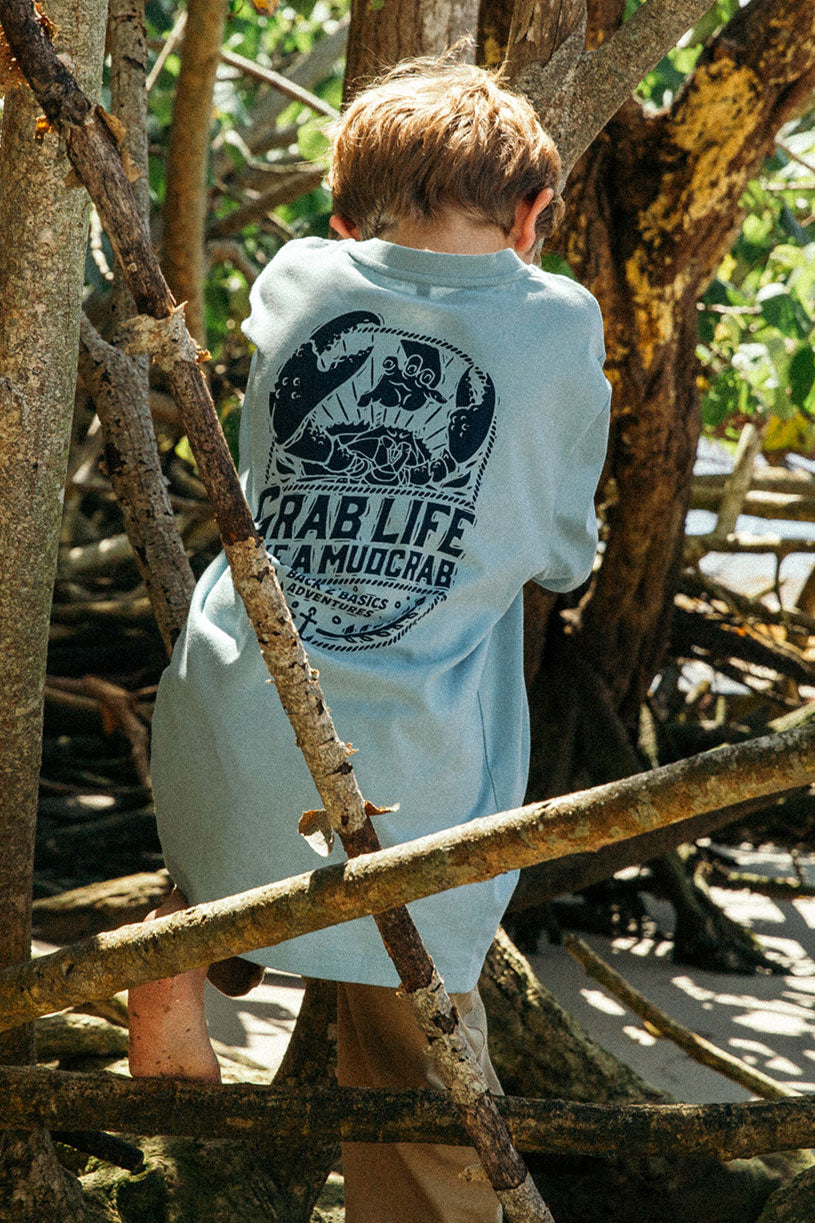 young boy wearing a back 2 basics grab life like a mudcrab tee shirt in blue at the beach back print