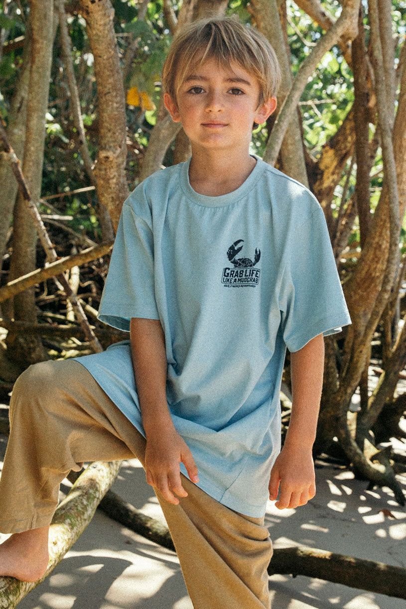 young boy wearing a back 2 basics grab life like a mudcrab tee shirt in blue at the beach