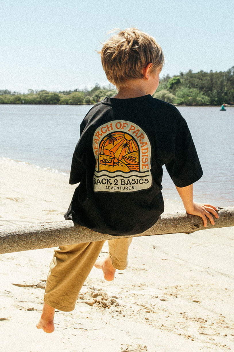 child at the beach searching for crabs in a black b2b kids in search of paradise tee