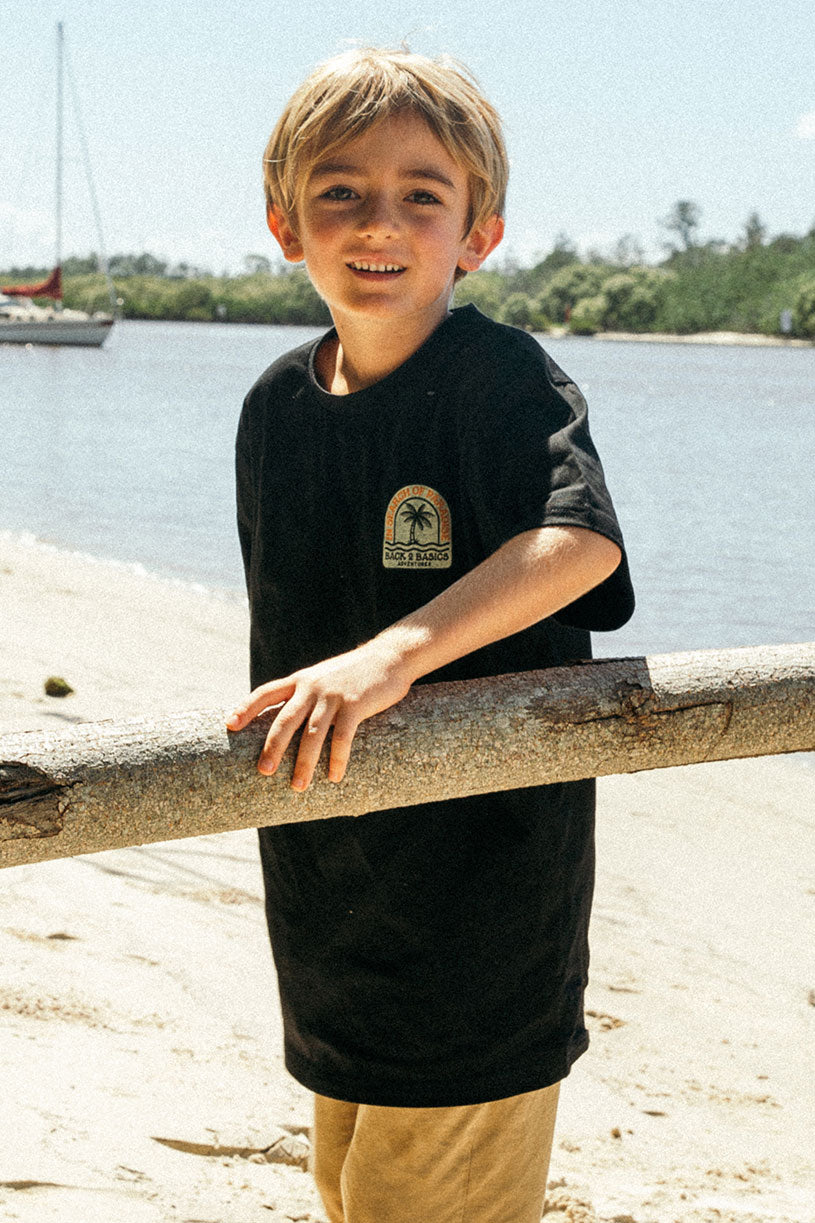 child at the beach searching for crabs in a black b2b kids in search of paradise tee