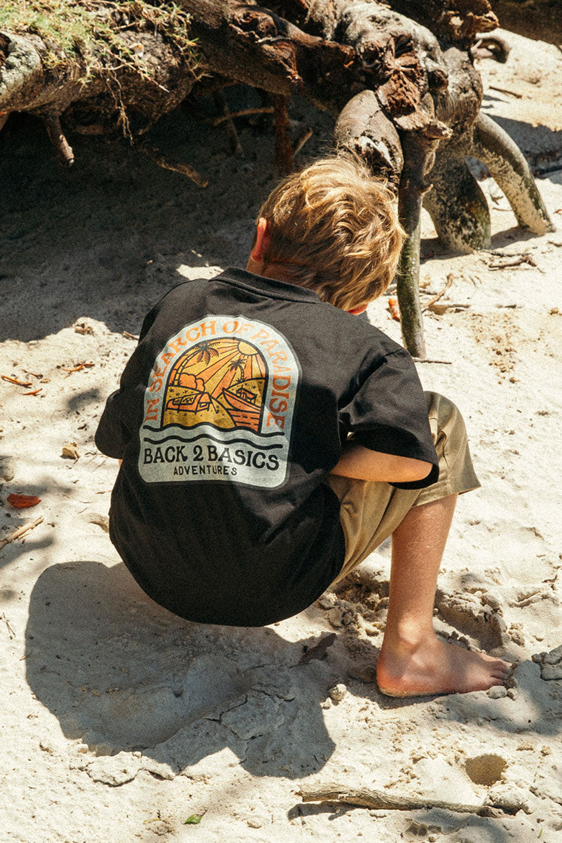 biy at the beach searching for crabs in a black b2b kids in search of paradise tee