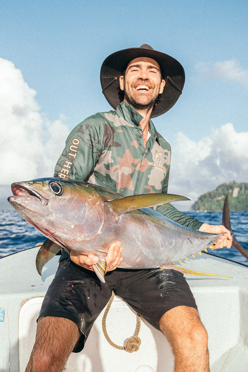 az from back 2 basics in a camo fishing jersey holding up a large yellow fin tuna caught on a fishing boat